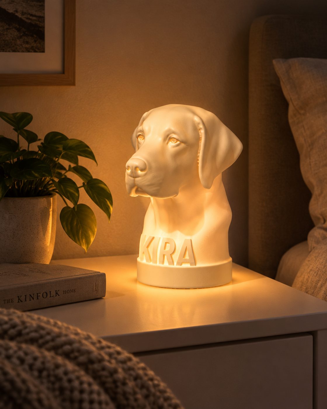 A white 3D-printed Labrador head lamp with KIRA on its base, glowing warm on a bedside table at night